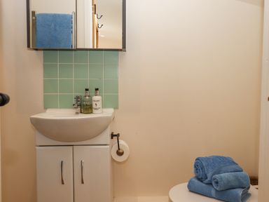 A small bathroom sink with green tiles a mirror and blue towels on a stool at The Wheelhouse Beacon near Yarcombe