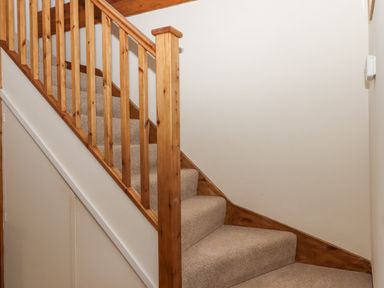A carpeted staircase with wooden railing and beige walls at The Wheelhouse Beacon near Yarcombe
