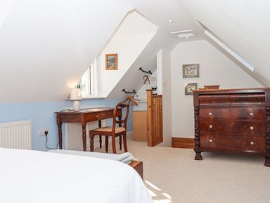 An attic bedroom with a wooden desk and chair near a window and a wooden dresser at The Wheelhouse in Beacon near Yarcombe