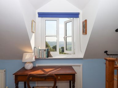 A wooden desk with a lamp and books by a window showing a countryside view at The Wheelhouse in Beacon near Yarcombe