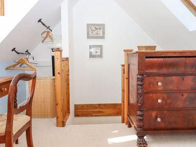 An attic landing area with a wooden chest of drawers a wooden chair a hanging rail with clothes hangers and a small framed pictures on the wall at The Wheelhouse Beacon near Yarcombe