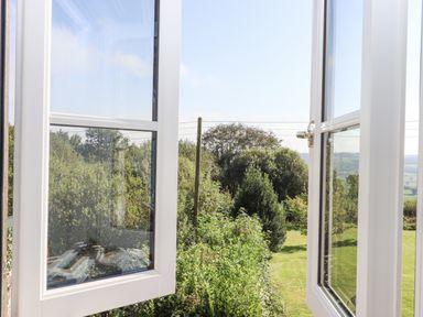 An open window looking out onto a garden with trees and grassy lawn at The Wheelhouse Beacon near Yarcombe