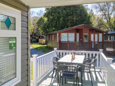 A balcony with a table and six chairs outside a wooden cabin at White Cross Bay near Troutbeck Bridge