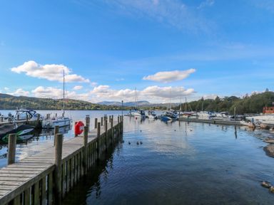A wooden dock extending into a lake with boats moored alongside and hills in the background at White Cross Bay near Troutbeck Bridge