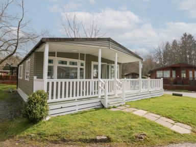 A cabin with a covered porch and white railing in a grassy area at Cosy Corner in White Cross Bay near Troutbeck Bridge