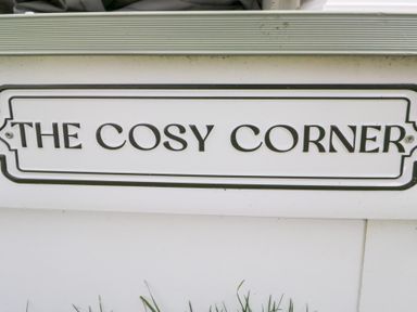 A sign reading THE COSY CORNER on a white background at Cosy Corner White Cross Bay near Troutbeck Bridge
