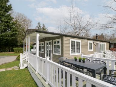 An outdoor deck with a table and chairs attached to a single-story house with white railing at Cosy Corner in White Cross Bay near Troutbeck Bridge