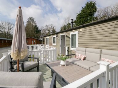Outdoor deck area with gray cushioned seating a wooden table white railing and a closed umbrella at Cosy Corner in White Cross Bay near Troutbeck Bridge