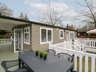 An outdoor deck area with a black table and chairs and a building with grey siding and white trim at Cosy Corner in White Cross Bay near Troutbeck Bridge