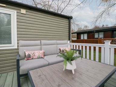An outdoor seating area with a gray sofa and pink cushions next to a wooden table with a plant on it at Cosy Corner in White Cross Bay near Troutbeck Bridge