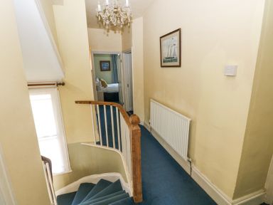 A hallway with a staircase carpeted in blue and a painting on the wall at Hereford House in Tenby