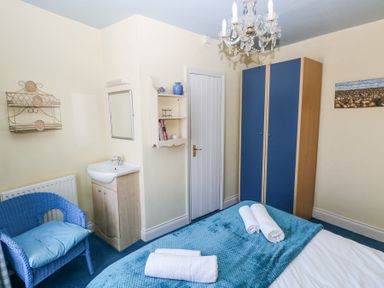 A bedroom with a bed, blue wardrobe, blue chair, small sink, and wall shelves at Hereford House in Tenby