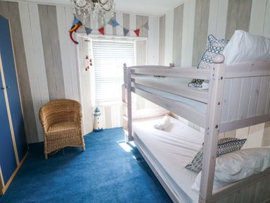 A bedroom with bunk beds a wicker chair a blue carpet and a window with blinds at Hereford House in Tenby