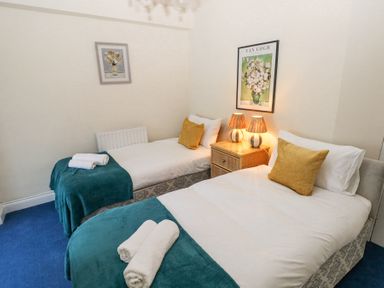 A bedroom with two single beds with yellow cushions and teal throws at Hereford House in Tenby