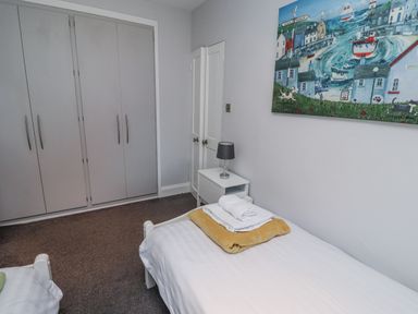 A bedroom with a bed, wardrobe, and side table at Kennie Cottage, Seahouses