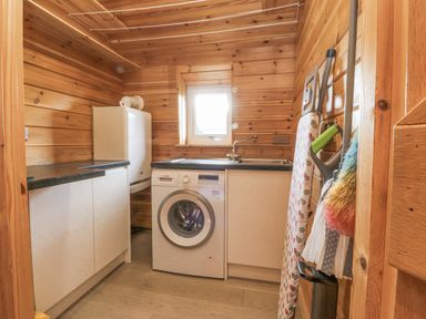 A laundry room with a washing machine refrigerator ironing board and cleaning tools at Artisan Lodge in Longridge