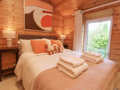 A bedroom with a bed with pillows and folded towels and wooden walls at Artisan Lodge in Longridge