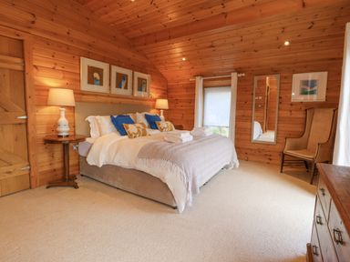 A bedroom with a large bed pillows and lamps wooden walls and ceiling a full length mirror and an armchair at Artisan Lodge in Longridge