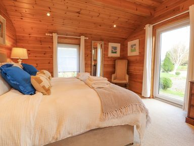A bedroom with a bed with blue and beige pillows a chair wooden walls and large glass door at Artisan Lodge in Longridge