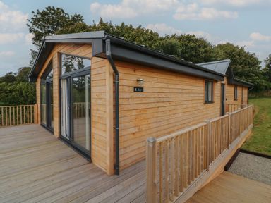 A wooden cabin with large glass doors and a wooden deck surrounded by trees at Bay in Ilfracombe