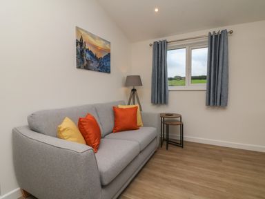 A sitting room with a gray sofa and colored cushions next to nested side tables and a window at Bay in Ilfracombe