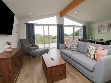 A living room with a grey sofa and patterned armchair next to sliding glass doors opening to a deck at Bay in Ilfracombe