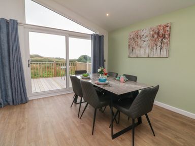 A dining area with a table and six chairs next to a glass sliding door overlooking a wooden deck at Bay in Ilfracombe
