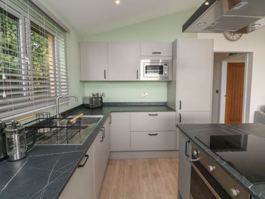A kitchen with grey cabinets black countertops a sink microwave toaster and stovetop at Bay in Ilfracombe