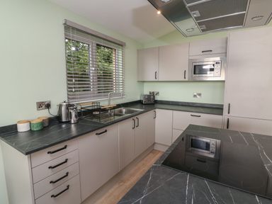 A kitchen with black marble countertops white cabinets a microwave a toaster a kettle and a window with blinds at Bay in Ilfracombe