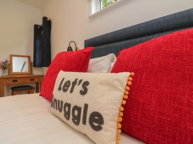 A bedroom with a bed featuring red pillows and a beige pillow with text a wooden vanity with a mirror and flowers at Bay in Ilfracombe