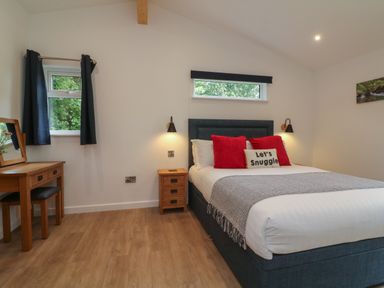 A bedroom with a bed with red cushions and a side table and a wooden dressing table at Bay in Ilfracombe
