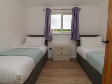 A bedroom with two single beds a three drawer nightstand and a window with purple curtains at Bay in Ilfracombe