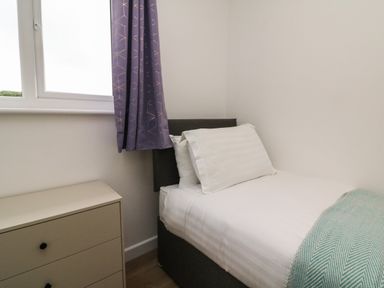 A small bedroom with a single bed next to a window and a beige chest of drawers at Bay in Ilfracombe