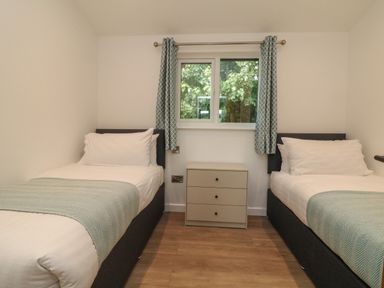 A bedroom with two single beds and a small chest of drawers under a window with curtains at Bay in Ilfracombe