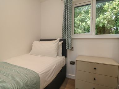 A small bedroom with a single bed a bedside table and a window with patterned curtains at Bay in Ilfracombe
