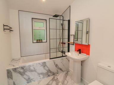 A bathroom with a bathtub shower combination a pedestal sink a toilet and a window at Bay in Ilfracombe