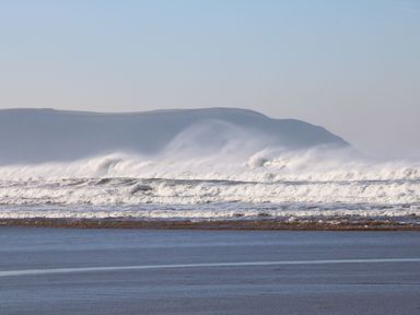 Waves crashing on a beach with hills in the background at Bay in Ilfracombe