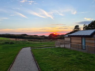 A gravel path leading to a wooden building with a metal roof during sunset at Cove Lodge in Ilfracombe