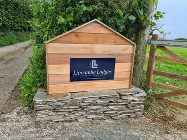 A wooden sign for Lincombe Lodges on a stone base near a country gate