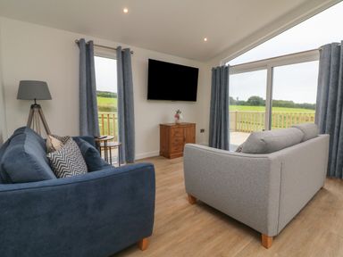 A living room with two sofas a TV on the wall and large windows with blue curtains at Cove Lodge in Ilfracombe