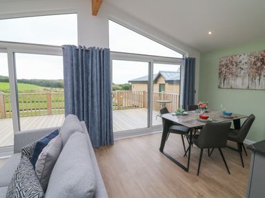 A dining area with a table set for four and a sofa near large sliding glass doors opening to a wooden deck at Cove Lodge in Ilfracombe