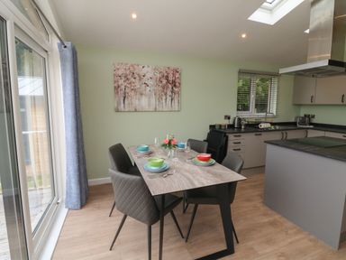 A dining table with four chairs set with colorful bowls and utensils in a kitchen with cabinets and a window at Cove Lodge in Ilfracombe