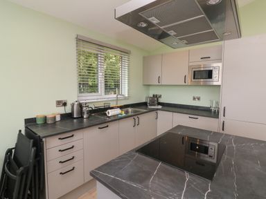 A kitchen with black countertops white cabinets a window with blinds and a built in microwave at Cove Lodge in Ilfracombe
