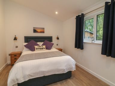 A bedroom with a double bed two purple pillows a small pillow with text two bedside tables and a window with dark curtains at Cove Lodge in Ilfracombe