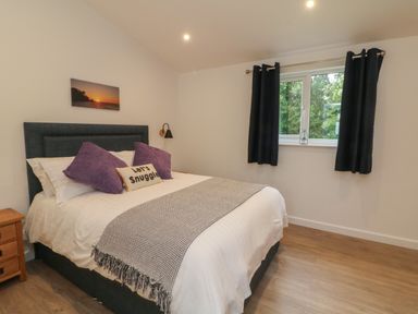 A bedroom with a double bed purple pillows and a window with black curtains at Cove Lodge in Ilfracombe