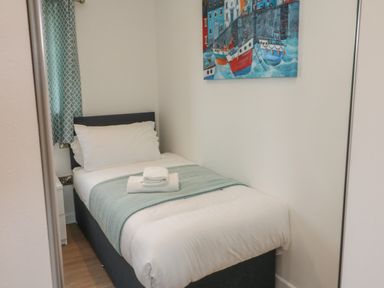 A single bed with white linens and a folded towel on top in a small bedroom at Cove Lodge in Ilfracombe