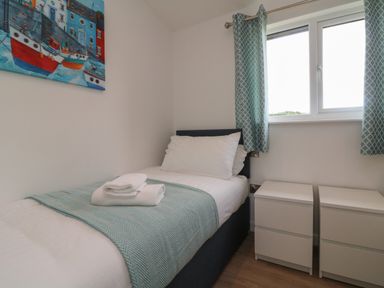 A small bedroom with a single bed two bedside cabinets and a window with blue curtains at Cove Lodge in Ilfracombe