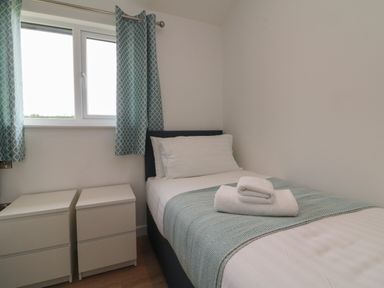 A bedroom with a single bed with folded towels on it two bedside tables and a window with patterned curtains at Cove Lodge in Ilfracombe