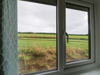A view of green fields through a window with a blue patterned curtain at Cove Lodge in Ilfracombe