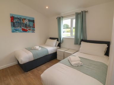 A bedroom with two single beds a window with curtains and a colorful painting on the wall at Cove Lodge in Ilfracombe